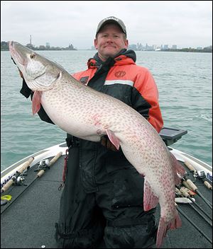 With the Windsor, left, and Detroit, right, skylines in the background fishing guide Jon Bondy shows off a muskie that he was able to catch with his homemade 