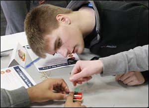 Alec Martinez, 17, of Swanton peers at his group’s electric motor as they work to construct it using a battery, magnet, and wires during the SSOE Group’s annual Engineer for a Day program. The group talked with students from An­thony Wayne, Bow­sher, Fosto­ria, and Swan­ton high schools on Wednesday about opportunities in different types of engineering careers.