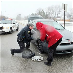 Toledo Police officer James Mrkva helps Bethany Pavy change a tire. She said she hit a big pothole the previous night and did not realize it flattened her tire until another motorist flagged her down in her morning commute. This winter's freezing and thawing has left many city streets pockmarked.