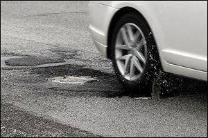 A car hits one of the deep potholes just off the Washington Street exit on southbound I-75 in Toledo. This winter has been hard on the roads.