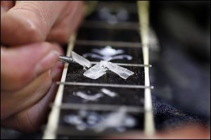 A craftsman removes the excess wax around the inlays on an ebony neck.