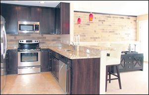 The efficient kitchen is perfectly on-trend with its hues of chocolate and silver, accented by a granite  countertop and red pendants.