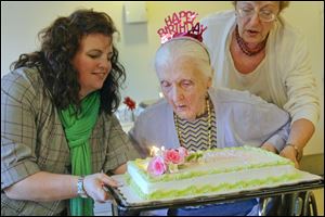 Social worker Karalyn Kibbey, left, and Tanya Borochin of Sylvania, right, hold Ella Goncharskaya’s  birthday cake as  Mrs. Goncharskaya blows out the candles Thursday at the Arbors of Sylvania.