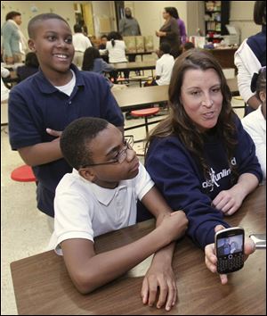 Heidi Burkhart shows a photo on her phone to kids at the Kids Unlimited charity office located inside Rosary Cathedral school in Toledo. Near her is Jerome Morgan, standing, and Brian Staples.