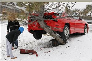 Tyler Shoup of Toledo bends to get a look at  Barry Conley's car after Conley (behind tree) of Bowling Green, crashed into a tree while exiting I-75 onto Erie Street in Toledo.