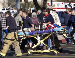 FILE - In this Jan. 8, 2011 file photo, Emergency personnel and Daniel Hernandez, an intern for U.S. Rep. Gabrielle Giffords, second right, move Giffords after she was shot in the head.