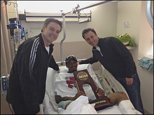 Injured Louisville guard Kevin Ware was brought the trophy from Sunday’s win by coach Rick Pitino, left, and former team assistant coach Richard Pitino.