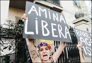 A Femen activist holds up a poster with writing reading in Italian 