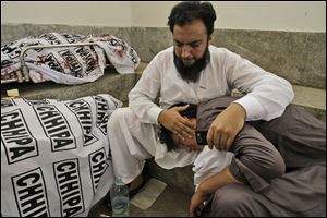 A Pakistani man comforts a family member next to the body of their relative who was killed in a bomb blast near a polling station on election day, at a hospital morgue in Karachi, Pakistan.