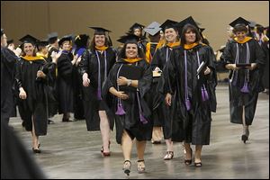 Janenne Marcus, of Monclova Township, center, clutches her degree as she and other recent graduates pass two lines of clapping faculty after the Lourdes University commencement.