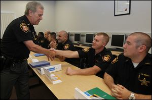 Lucas County Sheriff John Tharp, left, shakes the hand of Corrections Officer Joseph Rowland, as he thanks the officers on Monday during the first day of peace officer training at Owens Community College. Officer Matthew Grant, right, looks on. It’s the first class to have to pay its own way.