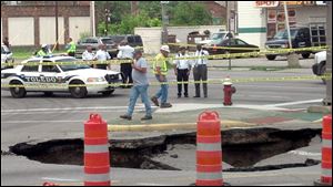 Mayor Mike Bell, far right, examines a large sinkhole that developed on North Detroit Avenue, swallowing a car and its driver. 