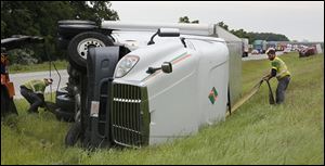 Jason Rodenberger, left, and Jason Hiser remove an overturned semi truck from the median of southbound I-75 near Cygnet, Ohio. State troopers said seven trucks were overturned by high winds from the storm.