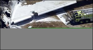 In this Saturday, July 6, 2013 aerial photo, a firefighter, right, stands by a tarpaulin sheet covering the body of a Chinese teen struck by a fire truck during the emergency response to the crash of Asiana Flight 214 at the San Francisco International Airport in San Francisco.