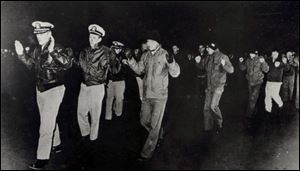 In this photo released by the U.S. Navy, crew members of the USS Pueblo hold up their hands in captivity in North Korea in 1968.