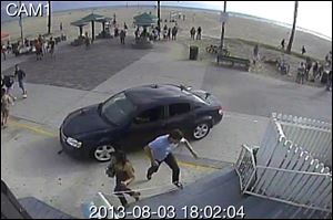 In this image take from a security camera, pedestrians scatter as a car drives through a packed afternoon crowd along the Venice Beach boardwalk Saturday in Los Angeles.