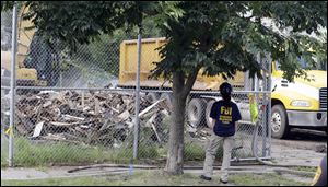 An FBI agent watches as the house where three women were held captive and raped for more than a decade is demolished in Cleveland today.