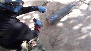 In this image taken from amateur video posted online, appearing to show a presumed U.N. staff member measuring and photographing a canister in the suburb of Moadamiyeh in Damascus, Syria, Monday.