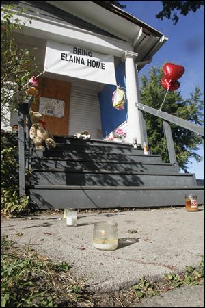 Lit candles join toys, balloons, and signs outside of the house at Federal and Leonard streets in East Toledo. This house is alongside the gathering site used by searchers for Elaina.