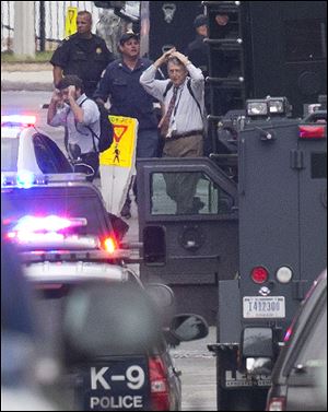 People hold their hands to their heads as they are escorted out of the building where a gunman was reported today at the Washington Navy Yard in Washington.