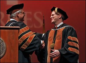 Thomas Geiger, left, shakes hands after presenting the medallion during Sunday’s inauguration of the ninth president of Lourdes University, David Livingston, at the Franciscan Center in Sylvania, Ohio.