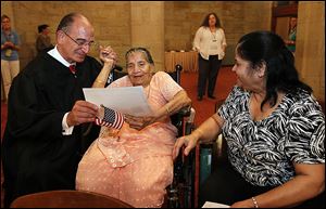 U.S. District Court Judge Jack Zouhary, left, presents Shardaben Chimanlal Vyas, 86, with her citizenship papers during the ceremony Thursday in Toledo. At right is her daughter-in-law, Anila Vyas. The elder Ms. Vyas lives with her son, Mahendra, and his family. She is a native of India. 