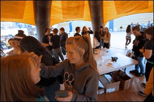 Alli Russell, 15, center, laughs as she paints Tiffany Orth, 15, in the Army tent in the field house at Whitmer High School.