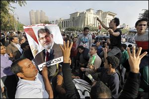 Supporters of Egypt's ousted President Mohammed Morsi raise their hands with four raised fingers, which has become a symbol of the Rabaah al-Adawiya mosque, where Morsi supporters had held a sit-in for weeks that was violently dispersed in August, as one holds his poster during a protest against Morsi's trial in front of the supreme constitutional court in Cairo, Egypt, Monday, Nov. 4, 2013. Egypt's deposed Islamist president was brought from the secret location of his four-month detention to face trial today.