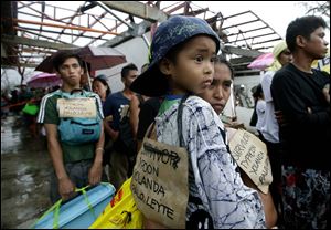 Typhoon survivors hang signs from their necks as they queue up in the hopes of boarding a C-130 military transport plane Tuesday in Tacloban, central Philippines. Thousands of typhoon survivors swarmed the airport on Tuesday seeking a flight out, but only a few hundred made it.