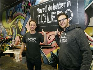 John Amato, left, and Josh Wagy display the winning slogan that won the Toledo Commerce Club’s competition in 1913. A much larger sign was first illuminated on Dec. 17, 1913, on top of the Valentine Theatre. The two created a pro-Toledo party  today at Wesley’s Bar & Grill, 1201 Adams St.