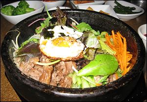 Korea Na's delicious bowl of dolsot bibim bap, a hot stone bowl full of rice, veggies, and a protein, is topped with an egg.