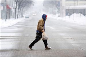 A lone man carries groceries across N. Michigan Street during a snowstorm on Sunday.