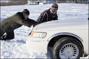 Mike Butzin, left, and Mark Oden of Point Place stop to help Marie Hayter, not pictured, of Temperance, Mich., get out of a snowbank where she was stuck on Suder Avenue near Lotus Drive in Erie, Mich.