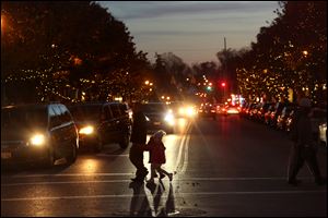 Pedestrians cross Main Street as downtown Sylvania's lights twinkle in the twilight during this winter's Downtown Delights in downtown Sylvania. Sylvania’s administration has been tasked with getting business owners’ perspectives on parking in downtown Sylvania.