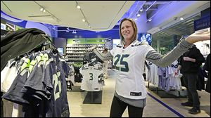 Ellen Kelly turns to a companion to help her decide as she tries on a Seattle Seahawks’ jersey at the team store in Seattle. New York City officials hope  Super Bowl XLVIII fans like Ms. Kelly will bring a steady stream of business when they converge on New York City for the big game Feb. 2. 