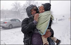 Brittany Cullard and her son, Michael Ferrel, 2, battle a wind-blown snow squall as they walk on North Huron Street in downtown Toledo on their way to the bus stop Monday.