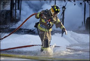 A Northwood firefighter carries a hose through water and ice while battling a house fire at 905 Gould Street in Northwood.