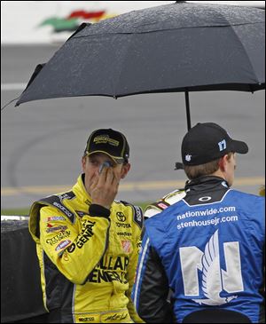 Matt Kenseth, left, looks out from under an umbrella as he stands near his car during a rain delay Sunday.