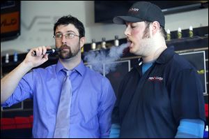 Manager Jordan Salkil, left, and sales clerk Austin Zaborowski ‘vape’ an ecigarette behind the counter at the Revolver Electronic Cigarettes & Vapor Lounge. 