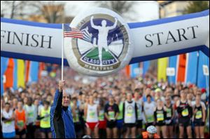 Tom Falvey holds the flag at the front of the starting line during the Medical Mutual Glass City Marathon today on the campus of the University of Toledo.