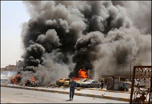 Iraqi policemen stand near burning vehicles moments after one in a series of bombs hit the Shiite stronghold of Sadr City, in Baghdad, Iraq, today.