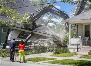 Walter Young, left, and Erica Besteder watch Toledo Streets, Bridges, and Harbor Division workers demolish a house at 660 Greene St. Ms. Besteder lives in the house at right.