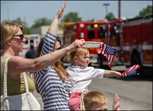 Kristina Ritenour, her daughter-in-law Amanda Ritenour, and Amanda’s daughter Anna, 2, wave to the passing fire trucks.