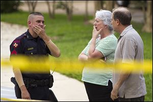 People stand with a law enforcement officer near the scene of a shooting in Spring, Texas. A Harris County Sheriff's Office statement says precinct deputy constables were called to a house about 6 p.m. Wednesday and found two adults and three children dead. Another child later died at a hospital. 