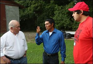 FLOC President Baldemar Velasquez, left, speaks with a migrant worker, who agreed to be photographed but declined to be named, center, outside the cinder block building where he lives.