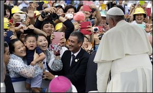 Pope Francis, right, blesses a crying child who is not wanting to separate from his mother, near a Vatican gendarmerie, center, upon the Pope's arrival for the Closing Holy Mass of the 6th Asian Youth Day on Sunday in Haemi, South Korea.