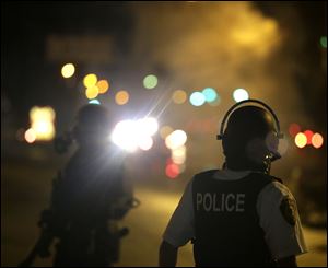 A law enforcement officer watches Sunday as tear gas is fired to disperse a crowd protesting the shooting of teenager Michael Brown.