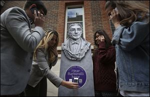 People listen to a talking statue on their phones at the launch of Talking Statues in central London, today. Statues of some three dozen historical and fictional characters in London and Manchester are coming to life thanks to a new interactive project that gives them a voice to tell their stories. Passers-by can swipe their smartphones on a tag or type in a web address to get an instant call from the characters depicted.