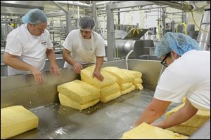 Adam Russell, an associate buyer for The Andersons, left, gets some guidance from Jacob Bulitz, center, as Mr. Russell and Lesley Kruzel, deli and seafood buyer for The Andersons, right, flip slabs of cheese during the cheddaring process at the Henning's Wisconsin Cheese.