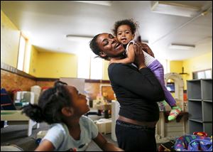 Nicole Barnes hugs daughter Camille Cain, 18-months, while playing with daughter Ta’Nyla Barnes, 5, at Family House. Ms. Barnes says knowing that her children learn while they are cared for will ease her mind as she rebuilds her life.